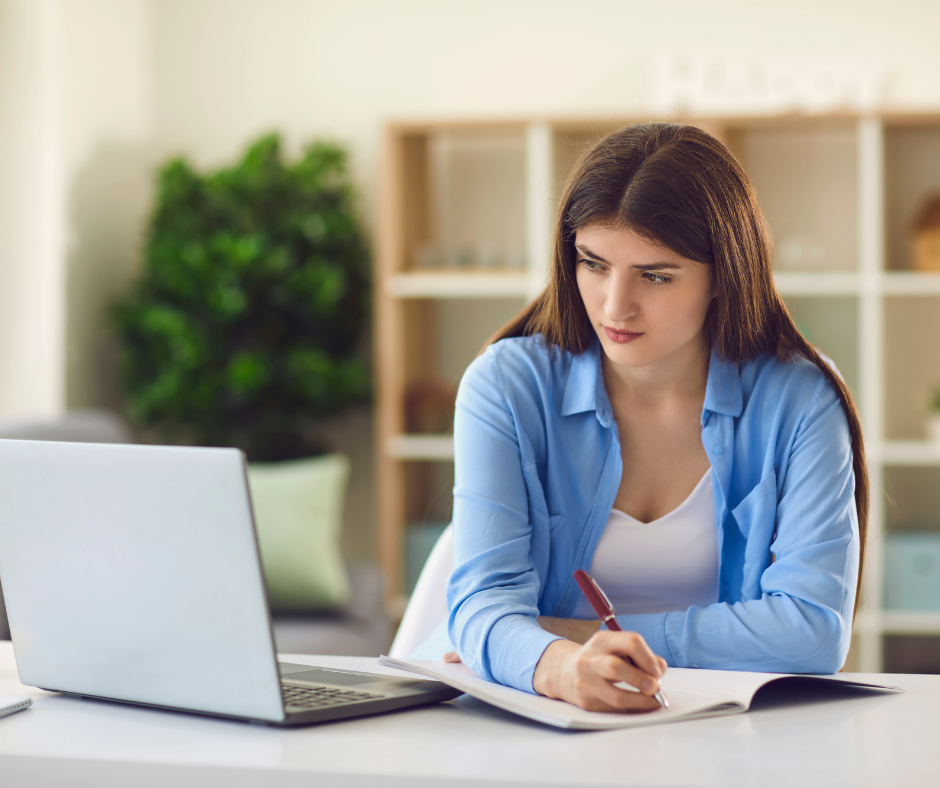 Zdjęcie poglądowe. Dziewczyna spogląda w ekran komputera i robi notatki.