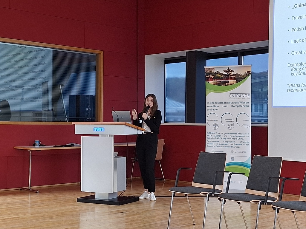 Kobieta stojąca z mikrofonem przy mównicy podczas wygłaszania prezentacji.