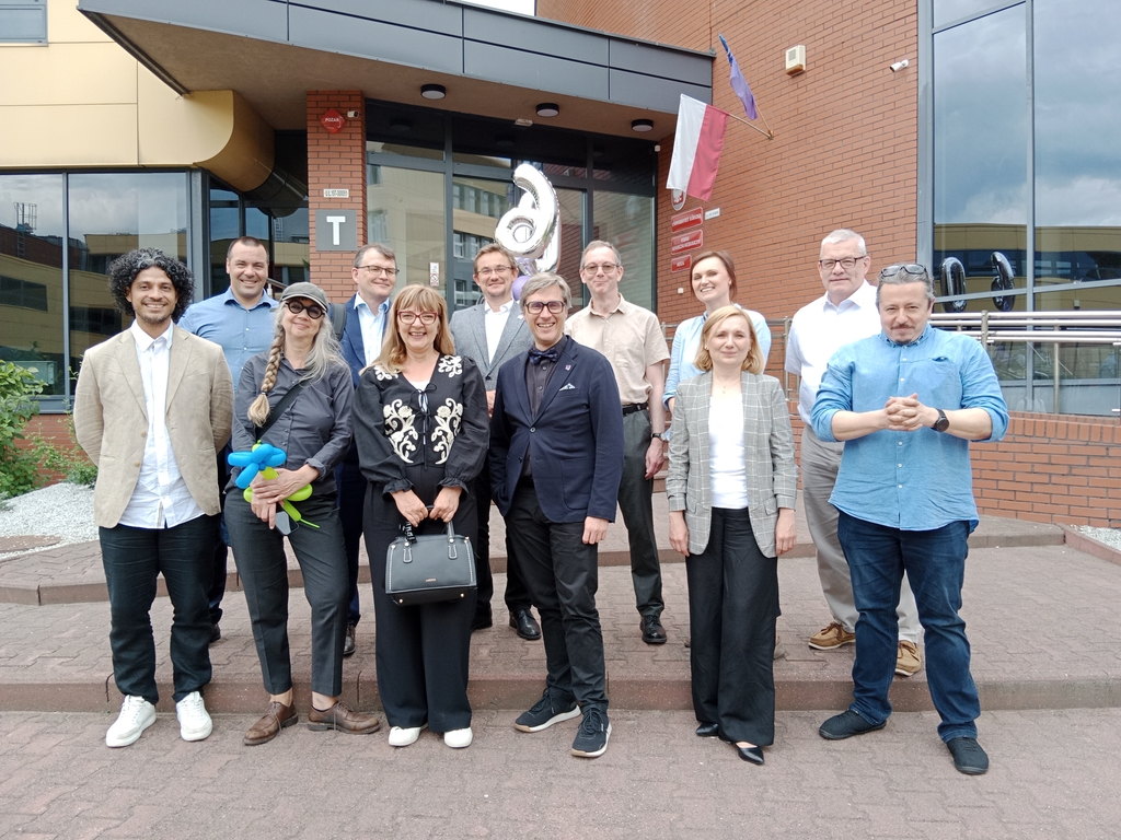 grupa uśmiechniętych ludzi w eleganckich strojach stojących przed budynkiem uniwersytetu