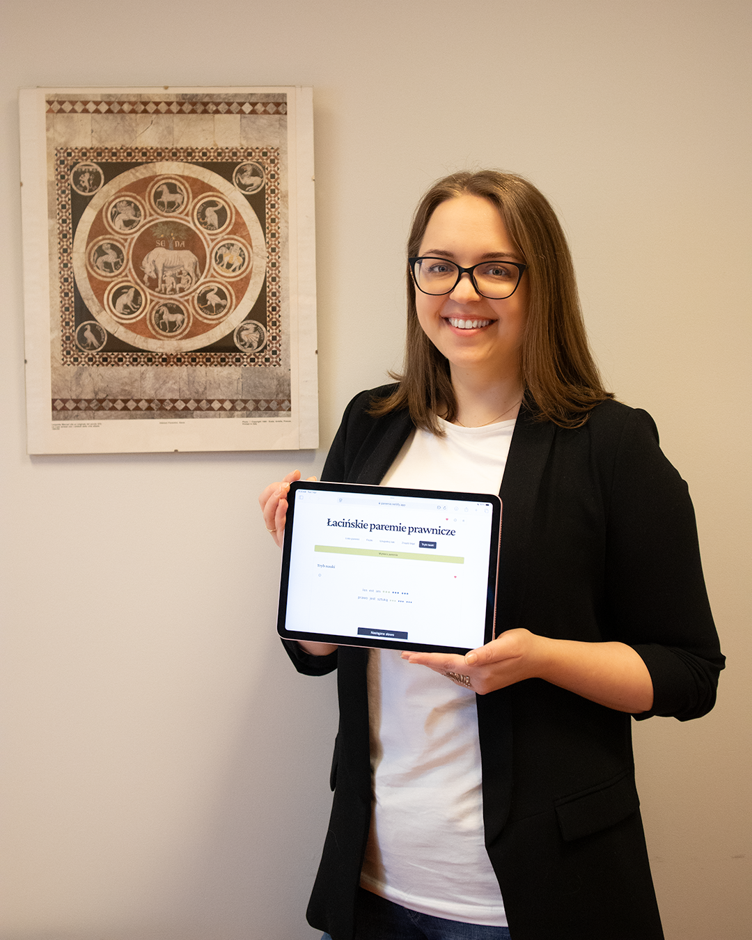 Kobieta o długich włosach ubrana w czarną marynarkę trzyma tablet.