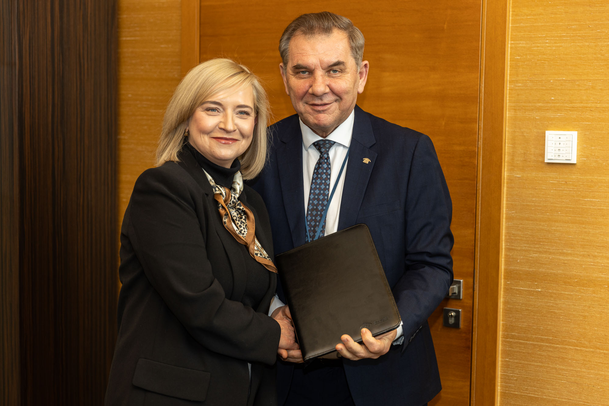 Blondwłosa kobieta w czarnym golfie i szpakowaty mężczyzna w grantowym garniturze