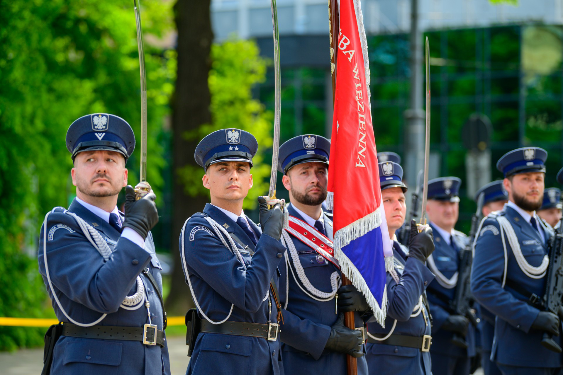 Służba Więzienna w galowych mundurach z szablami w dłoniach.