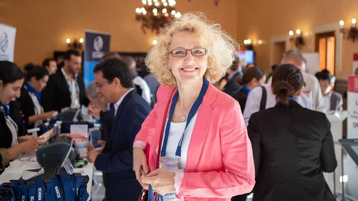 Blondynka w okularach na tle tłumu podczas konferencji.