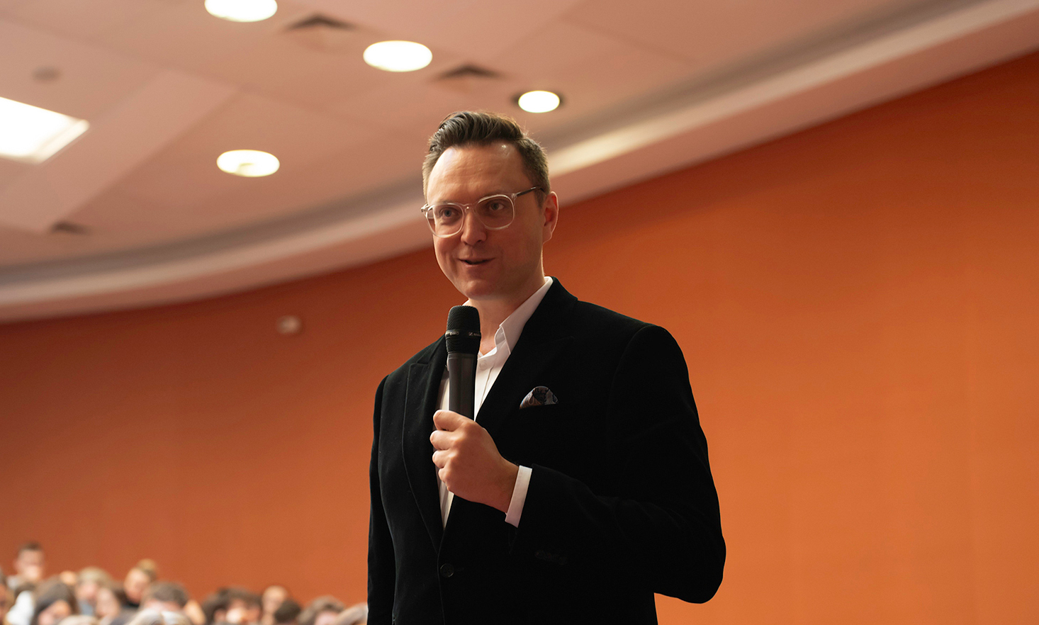 Mężczyzna w okularach trzymający mikrofon.