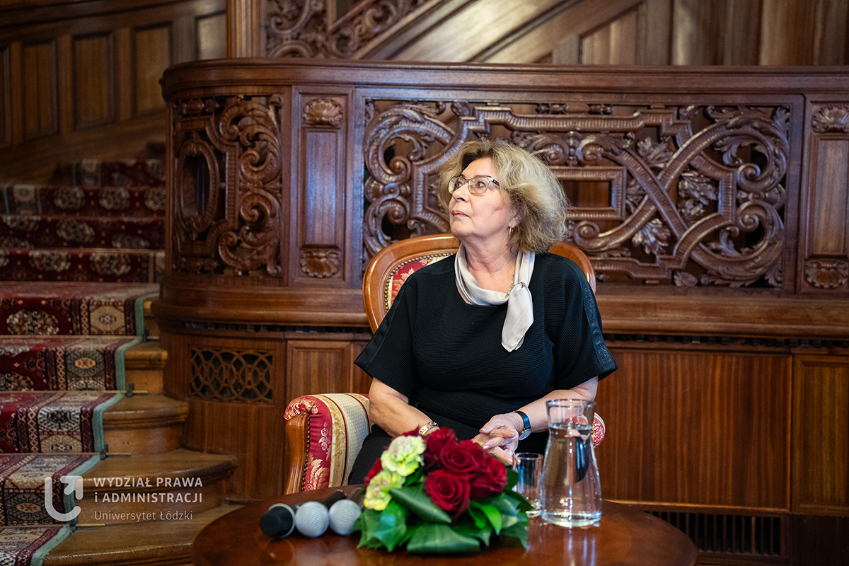 Blondwłosa kobieta w okularach siedząca na eleganckim krześle.