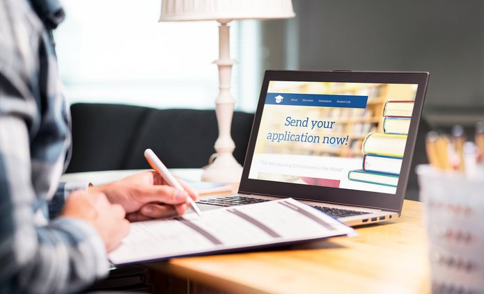 osoba pisząca w zeszycie przed komputerem