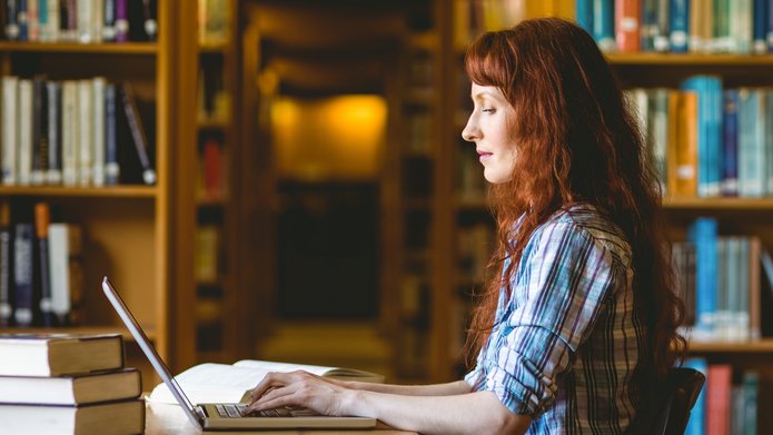 kolorowe zdjęcie przedstawia młodą studentkę pracującą w bibliotece