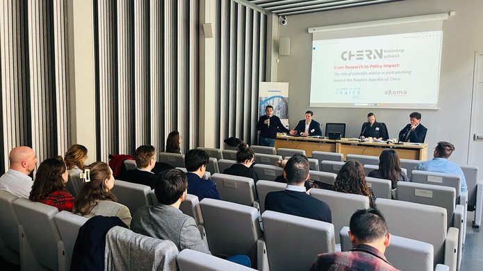 Grupa osób siedząca w sali audytoryjnej słuchająca wypowiedzi czterech panelistów