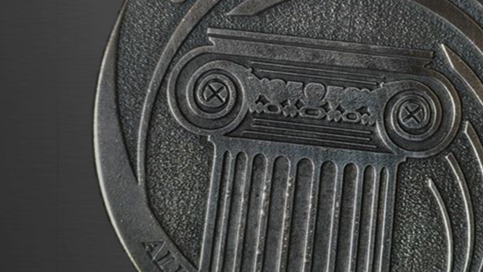 Okrągły medal metalowy z wytłoczonymi detalami: na górnej połowie napis „UNIVERSITAS LODZIENSIS” wzdłuż krawędzi. W centralnej części stylizowana kolumna dorycka z bogato zdobionym kapitelem. Na dolnej części medaliony wpisano sentencję „ALUMNO LAUDE DIGNISSIMO”. Tło reliefowe o drobnej fakturze podkreśla wyryte elementy – napisy i kolumnę.