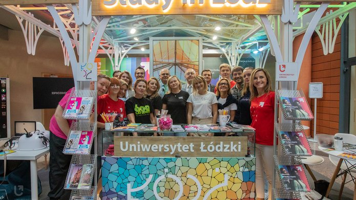 Grupa osób stojaca na stoisku z napisami Study in Lodz, Uniwersytet Łódzki, Uniwersytet Medyczny w Łodzi, Politechnika Łódzka