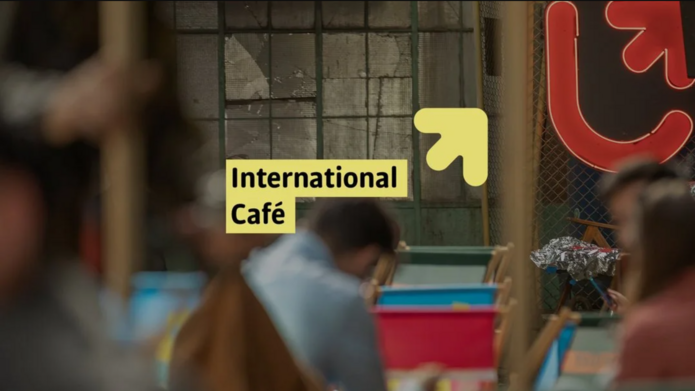 Zdjęcie przedstawiające zaludnioną przestrzeń z logotypem UŁ i logo International Café