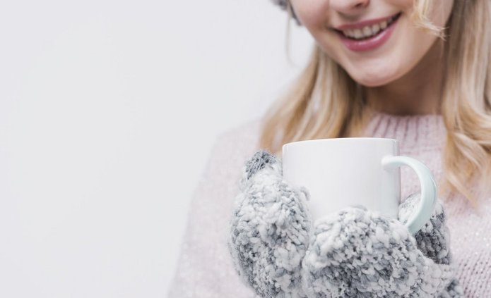 Zdjęcie: uśmiechnięta młoda kobieta w ciepłych rękawiczkach trzyma kubek
