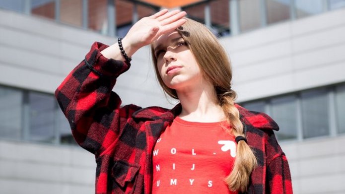 dziewczyna na tle WZ patrzy w stronę Słońca, osłania oczy