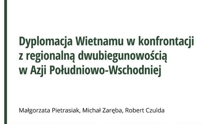 Okładka książki „Dyplomacja Wietnamu w konfrontacji z regionalną dwubiegunowością w Azji Południowo-Wschodniej”. Na okładce widoczna jest wąska kolejowa uliczka w gęsto zabudowanej części miasta w Wietnamie, z budynkami ozdobionymi flagami Wietnamu, roślinnością i muralami.