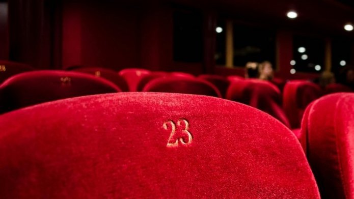 Zdjęcie poglądowe. Obite czerwonym materiałem krzesła w sali teatralnej, na jednym widoczny numer 23.