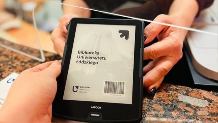 Czytnik e-booków przekazywany czytelniczce przez pracowniczkę wypożyczalni.