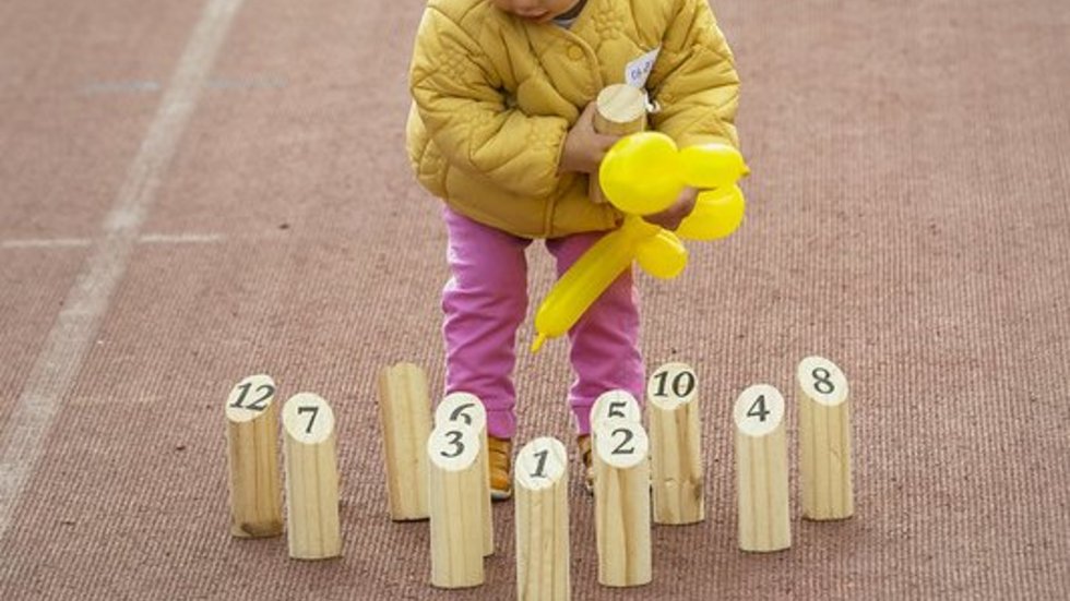 Dziecko z żółtym balonem, stojące wśród drewnianych zabawek