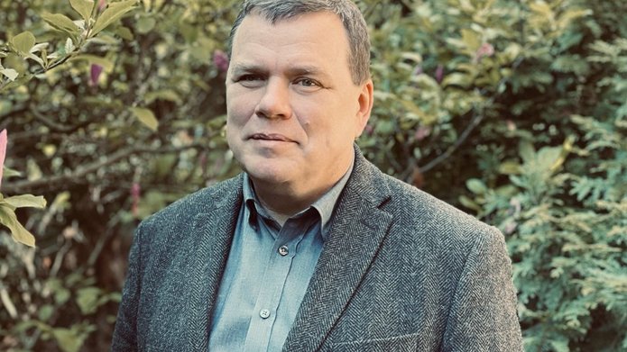 Tomasz Gwizdałła na tle zielonego krzewu