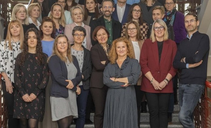 Duża grupa ludzi, kobiet i mężczyzn, stojących na schodach na klatce schodowej Uniwersytetu Łódzkiego.