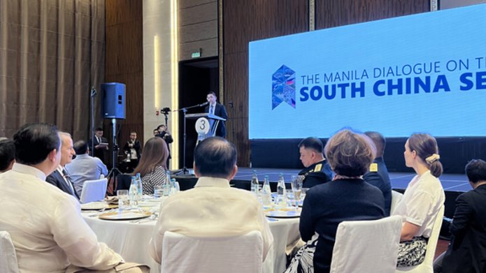 Mężczyzna stojący na mównicy na tle ekranu promującego konferencję "The Manila Dialogue on the South China Sea"