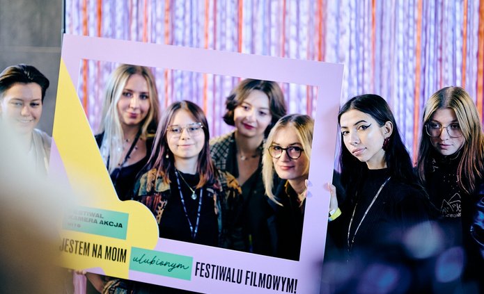 Grupa młodych osób pozuje do zdjęcia z ramką promocyjną Festiwalu Kamera Akcja 