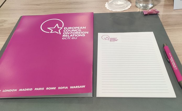 Stolik z teczką z napisem "European Council on Foreign Relations", notatnikiem oraz szklanką i butelką wody 