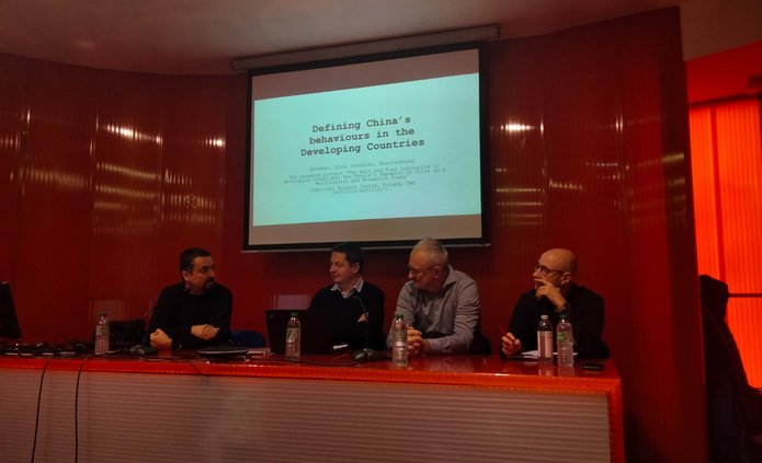 Czterech prelegentów siedzących przy stoliku a w w tle ekran z prezentacją z rzutnika