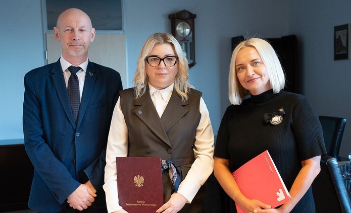 Trzy osoby trzymające teczki z podpisanym porozumieniem.