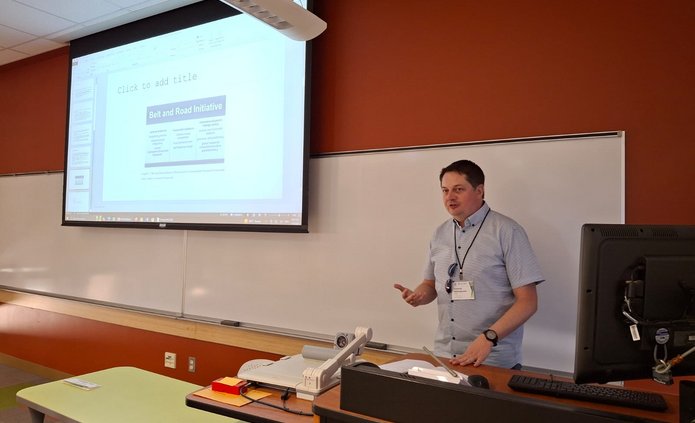 Prelegent wygłaszający przemowę na tle prezentacji wyświetlanej z rzutnika