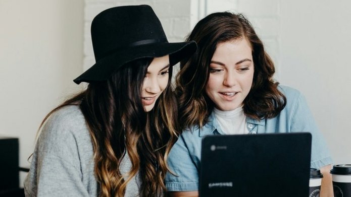 Zdjęcie poglądowe. Dwie uśmiechnięte dziewczyny wpatrzone w ekran laptopa.