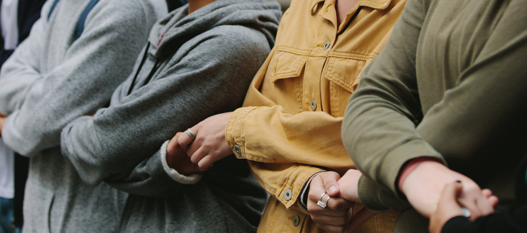 Sylwetki 4 osób stojących obok siebie i trzymających się za skrzyżowane ręce