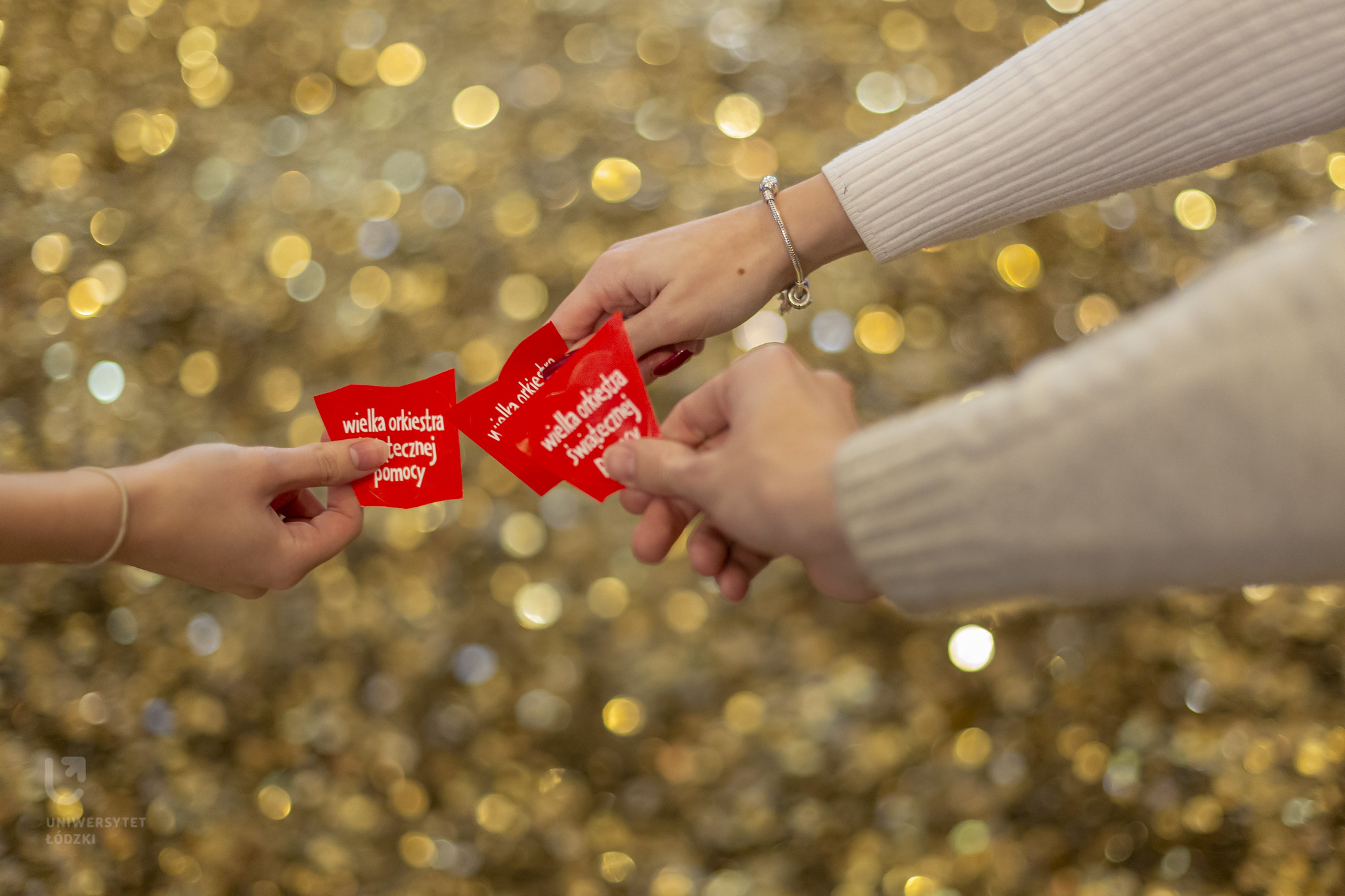 3 ręce trzymające czerwone serduszka z napisem Wielka Orkiestra świątecznej pomocy na tle złotych monet